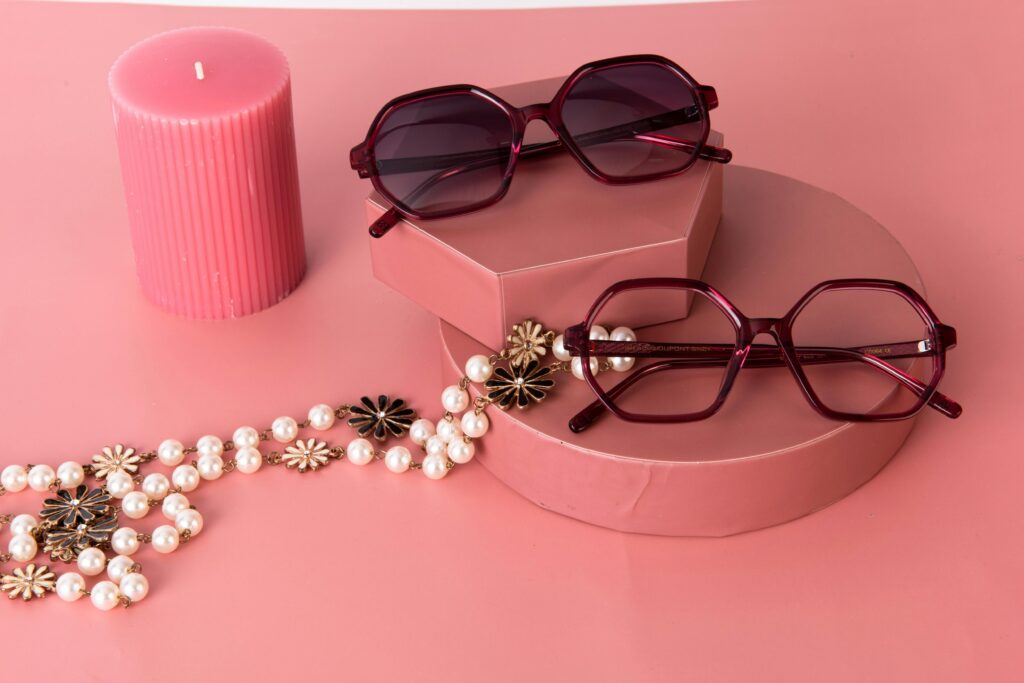 Chic sunglasses paired with pearls and a candle on pink backdrop, perfect for fashion aesthetics.
