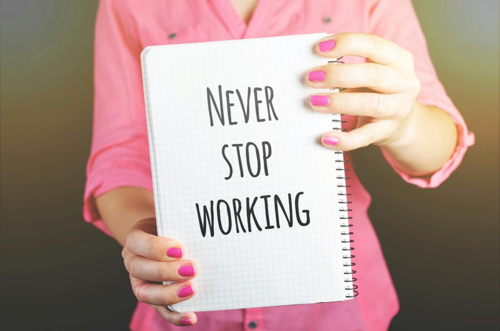 A woman holding a notebook with the motivational message 'Never Stop Working' indoors.